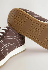 Baskets marron avec des lacets blancs, dotées d'une semelle en gomme texturée et de coutures blanches contrastantes. Design simple à bout rond.