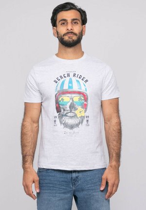 Homme barbu portant un t-shirt blanc avec un crâne portant un casque à rayures bleues, des lunettes de soleil réflectives montrant des palmiers, et une fleur jaune dans la bouche.