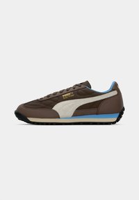 Braune Puma Easy Rider Sneaker mit beiger Streifen, blauen Akzenten, schwarzer Sohle und Schnürdesign, von der Seite auf einem weißen Hintergrund gezeigt.