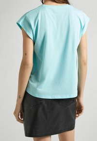 Ljusblå bomullströja med rullade ärmar, tillsammans med en svart fusk läder mini kjol med bakfickor och en slät yta.