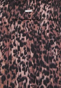 Tessuto plissettato con stampa leopardata marrone e nera e dettagli in script neri sottili, con una piccola etichetta rettangolare argentata vicino alla parte superiore.