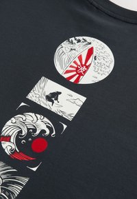 Tissu noir avec des motifs blancs et rouges représentant des vagues stylisées, un surfeur et une planche de surf avec des rayons rouges et un symbole blanc.
