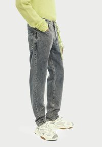 Szare dżinsy z denimu o luźnym kroju, z detalem w postaci zielonego sznurka i subtelnymi ozdobnymi przeszyciami po bokach.