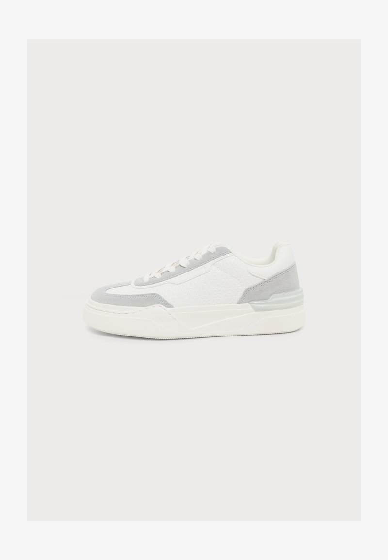Λευκό χαμηλό sneaker με ανοιχτό γκρι σουέτ λεπτομέρειες και παχύ λευκό πάτο, εμφανίζεται από το πλάι σε απλό φωτεινό φόντο.