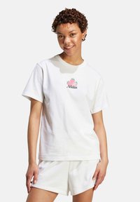 Vit bomull t-shirt med rund hals och korta ärmar, med en rosa ananas och "Adidas"-logotyp i grönt.