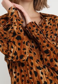 Camicia button-up marrone con grande stampa leopardata nera, caratterizzata da un tessuto testurizzato e dettagli a forma di stella sui bottoni dei polsini.