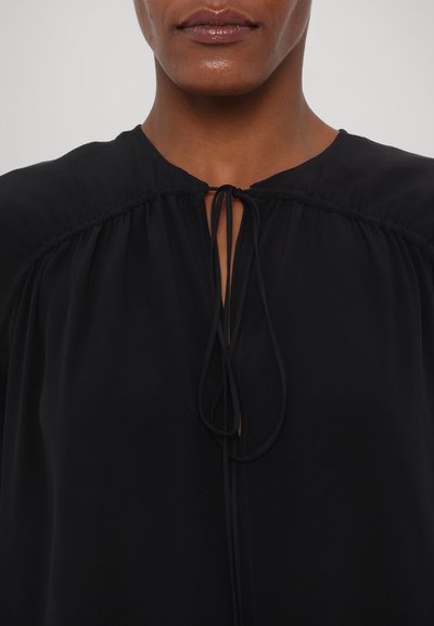 Blusa nera con un'apertura a fissaggio al collo, dettagli arricciati sulle spalle e un tessuto liscio e leggero.