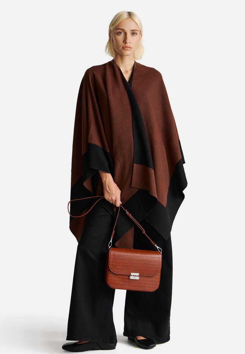 Poncho marrone e nero con una texture liscia, caratterizzato da un design geometrico. Si tiene una borsa a tracolla con effetto coccodrillo marrone, dotata di una chiusura argentata.