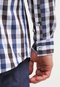Kostkovaná košile s modrými, hnědými a bílými vzory. Manžety na knoflíky, slim fit a lehká látka s hladkou texturou.
