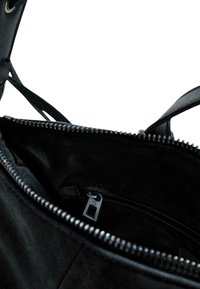 Schwarze Handtasche mit geöffnetem Reißverschluss, die ein leeres Innenleben und eine innere, mit Reißverschluss versehene Tasche mit einem Metallzugtab zeigt.