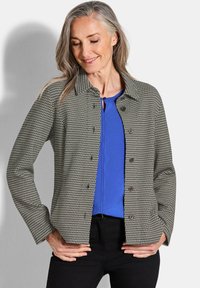Grijze en zwarte geruite blouse met een kraag, lange mouwen en voorzakken, gelaagd over een blauwe top.