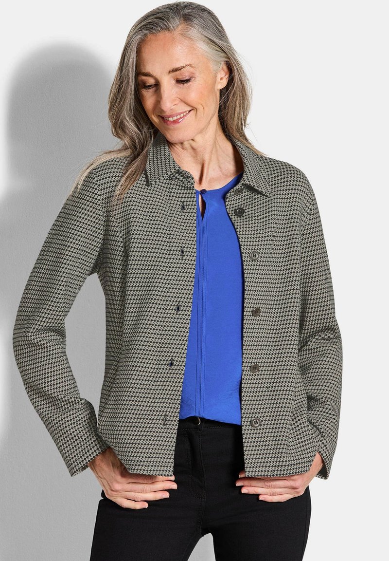 Grijze en zwarte geruite blouse met een kraag, lange mouwen en voorzakken, gelaagd over een blauwe top.