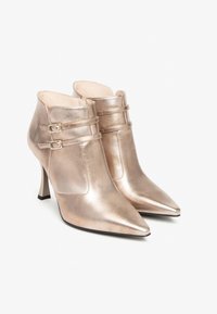 Metallic roségoldene Knöchelstiefel mit spitz zulaufenden Zehen, ausgestattet mit doppelten Schnallenakzenten und schmalen Absätzen. Glatte Ledertextur und elegantes Design.