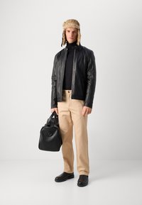 Sort læderjakke over en sort turtleneck, beige bukser, sorte sko og en sort taske. En pelsforet pilothat fuldender looket.