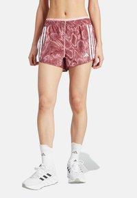 Rode shorts met slangenhuidmotief en witte accentstrepen, elastische tailleband en een sportief ontwerp, gecombineerd met witte sneakers en sokken.