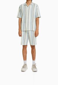 Camisa de botones de manga corta y pantalones cortos a juego, con rayas verticales azules, negras y grises sobre un fondo claro. Material de algodón.