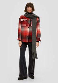 Rote und schwarze Karottenflanellhemden mit zwei Brusttaschen, kombiniert mit einem langen grauen Strickschal und schwarzen Schlaghosen. Schwarze Plateauschuhe.