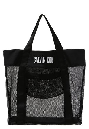 Schwarze Mesh-Einkaufstasche von Calvin Klein mit solidem schwarzem oberen Rand und Trägern, mit weißem Calvin Klein-Logo auf dem oberen vorderen Paneel.