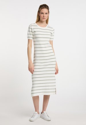 Femme portant une robe midi blanche avec de fines rayures horizontales vertes et des baskets blanches, debout avec une main le long du corps.