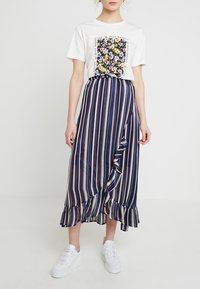 White t-shirt with a floral graphic, paired with a navy striped wrap skirt featuring ruffles. Worn with white shoes.
