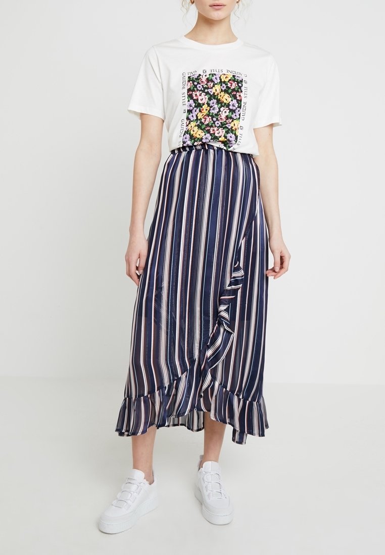 White t-shirt with a floral graphic, paired with a navy striped wrap skirt featuring ruffles. Worn with white shoes.