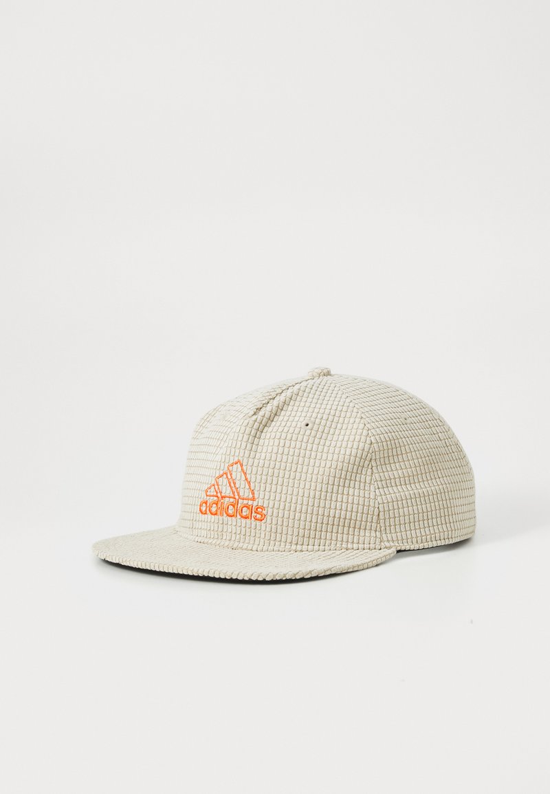 Beige baseball cap tekstuuriga, millel on oranž Adidas logo tikandiga ees, millel on lame ääre, esitatud valge tausta taustal.