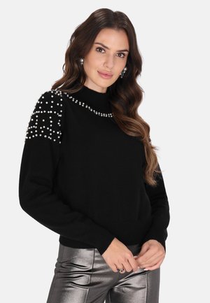 Pulover negru cu guler înalt, decorat cu strasuri mari pe umeri, asortat cu pantaloni metalici argintii.