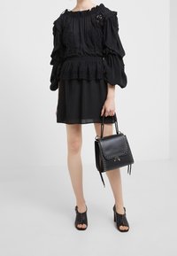 Musta peplum-pusero, jossa on pitsiyksityiskohtia, kerätty pääntie ja volyymiha sleeves, yhdistettynä niiteillä varustettuun mustaan käsilaukkuun ja avokärkisiin korkokenkiin.