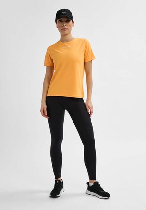 Lichtgewicht oranje sport T-shirt met korte mouwen, in combinatie met zwarte leggings en zwarte sneakers. Eenvoudig ontwerp en synthetische textuur.