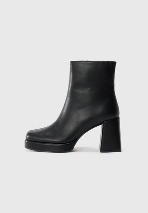 Bottine en cuir noir avec un talon bloc et une semelle plateforme, vue de côté sur un fond blanc uni.