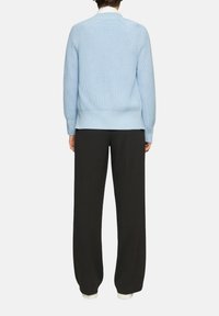 Hellblauer Strickpullover mit einem strukturierten Muster, geripptem Saum und Bündchen, kombiniert mit schwarzen weiten Hosen und weißen Schuhen.