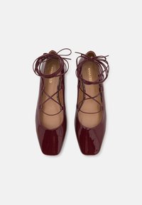 Burgundy patent leather flats with a square toe, featuring crisscross laces and a smooth texture. Lining is a light tan color.