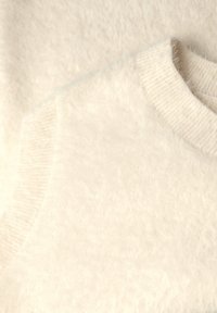 Tissu en tricot couleur crème avec une texture douce et pelucheuse. Comprend un col côtelé et des bords de manches lisses.