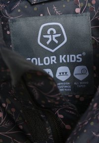 Tumša auduma ar ziedu rakstu rozā un zaļās krāsās. Etiķete rāda zīmola nosaukumu "COLOR KIDS" un norāda uz berzes izturību un šuvju līmēšanu.