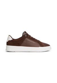 Low-top brown sneaker with white sole, lace-up front, Tommy Hilfiger logo on side and back, and white heel accent.