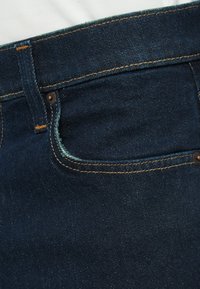 Tmavě modré džíny z denimu s přední kapsou, kontrastním žlutým šitím a měděným kováním. Mírné třepení u okraje kapsy.