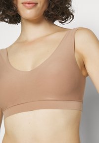 Lichtbruine bralette met een diepe V-halslijn, brede bandjes, naadloos ontwerp en zachte, rekbare stof voor comfort.