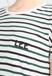 Chemise à manches courtes rayée avec des rayures horizontales vertes et noires. Dotée d'une poche avant avec le logo "LEE" en noir. Fabriquée en tissu léger.