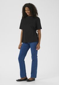 Black short-sleeve top with side ties, paired with blue straight-leg jeans and black flats. Smooth fabric, relaxed fit, and casual design.
