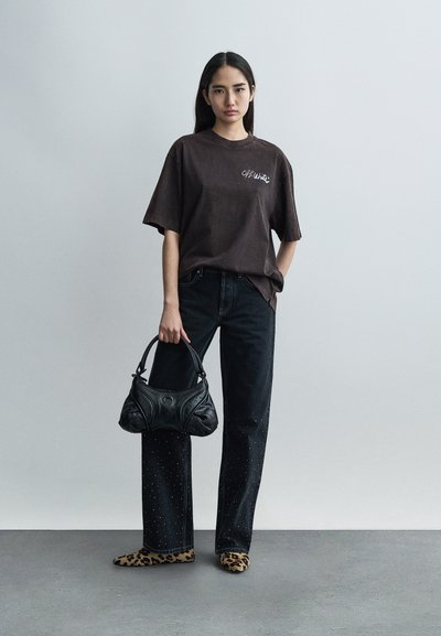 Σκούρο καφέ υπερμεγέθη μπλουζάκι με το λογότυπο "Off-White", συνδυασμένο με μαύρα τζιν με τρουκς, παπούτσια με τύπωμα λεοπάρδαλης και μαύρη τσάντα.