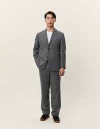 Γκρι ριγέ κοστούμι από υφασμάτινη ύλη με υφή. Μονόκουμπη σακάκι με πέτο, σε συνδυασμό με αντίστοιχους παντελονιού. Μαύρα παπούτσια.