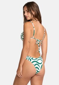Grön och vit mönstrad bikini, med justerbara axelremmar, en knytning i ryggen och en högskuren underdel med vågiga mönster.