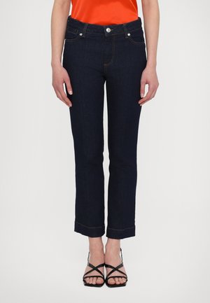 Donkerblauwe spijkerbroek met een rechte snit, vier zakken en opgerolde zoom; gecombineerd met zwarte sandalen met bandjes en een feloranje top.