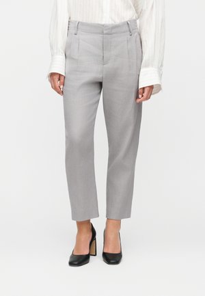 Kvinde iført lige, lysegrå, skræddersyede bukser kombineret med sorte høje hæle og en hvid langærmet skjorte.