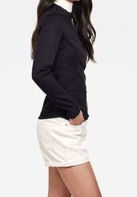 Giacca blu navy con zip e collo alla coreana, abbinata a pantaloncini bianchi. La giacca ha un design aderente e maniche lunghe.