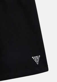 Czarna tkanina z małym trójkątnym wzorem błyszczących diamencików blisko dołu na jednolitym jasnym tle.