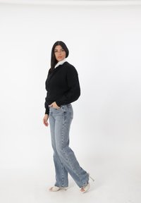 Maglione nero a maglia con maniche lunghe, camicia bianca con colletto sotto, jeans svasati blu chiaro e sandali beige con tacco alto.