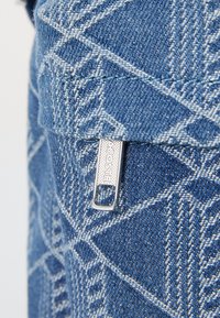 Blauwe denimstof met een geometrisch patroon, voorzien van een zilveren rits met een gestructureerde trekband en een merkaanduiding.