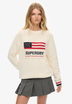 Kremowy sweter wykonany na drutach z motywem amerykańskiej flagi w kolorach czerwonym, białym i niebieskim oraz napisem "SUPERDRY". Paski na rękawach.