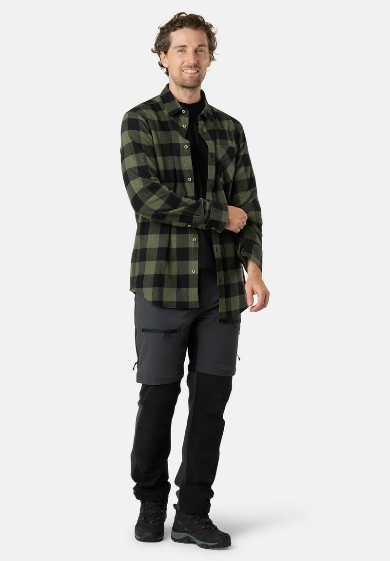 Grün-schwarz kariertes Flanellhemd mit Knöpfen, schwarzes T-Shirt darunter, graue Cargo-Shorts mit Reißverschlusstaschen und schwarze Wanderschuhe.